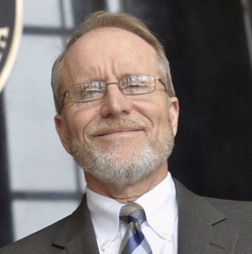 A cropped webpage screenshot showing a portrait of a person wearing a suit and tie on the left side, and a block of text on the right. The text describes a director of a cyber range and outlines work in cybersecurity education, hands‑on training for students, and a return to IgniteND to discuss infrastructure, access, and how AI shapes cybersecurity training scenarios.